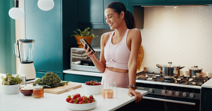 House, fitness and woman in kitchen, smartphone and smile with fruit, typing and online reading for diet. Person, apartment or athlete with sportswear, cellphone or nutrition with social media or app