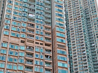 Fototapeta premium Dense Hong Kong apartment buildings rise high, showcasing numerous windows and balconies in a close-up view. The image highlights the architecture of these urban dwellings.
