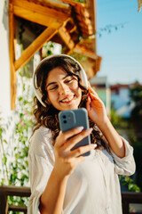 Young caucasian woman listening to music or audio book on her balcony	