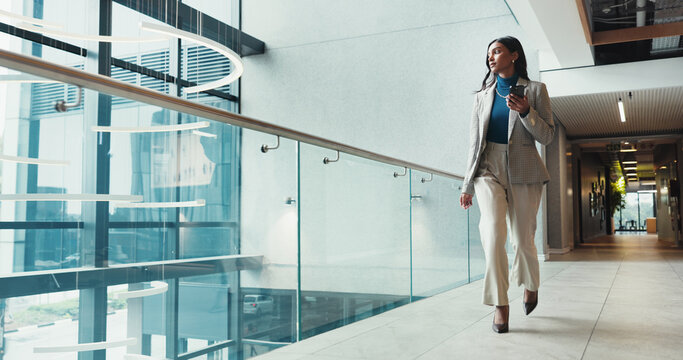 Corridor, phone and walking with business woman in office for arrival, communication or progress. App, social media and typing text message with Indian employee thinking in corporate workplace