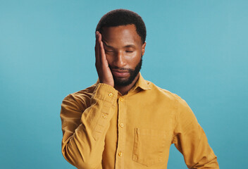 Stress, tired and black man with headache in studio, tension or pressure on blue background....