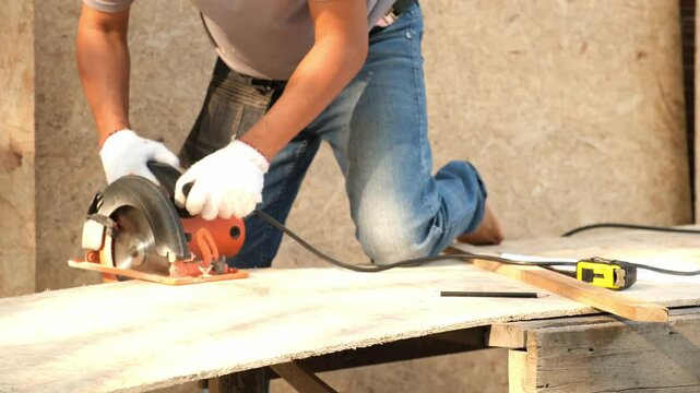 A carpenter man worker cuts wood panels plank with a circular saw to make or repair eco-friendly furniture.