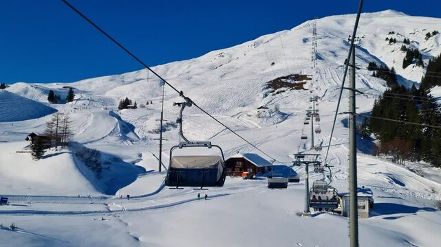 Chairlift shot in the Adelboden-Lenk ski area and view on a traditional chalet restaurant. Skiers glide down powdery slopesin the background under a blue sky