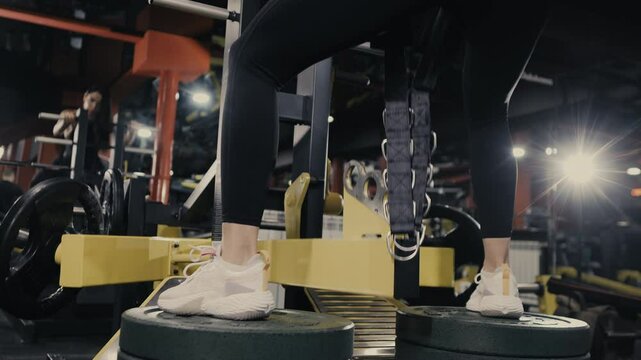 Close up of legs doing squat exercise on gym machine.