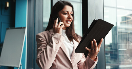 Finance, phone call and tablet with business woman at window in office for investment update. Asset management, conversation and wealth with employee trading on stock market for portfolio strategy