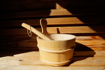 Sauna bench and water bucket with scoop in cedar sauna.  Sunlight on subject with dark shadows surrounding.   Close-up.