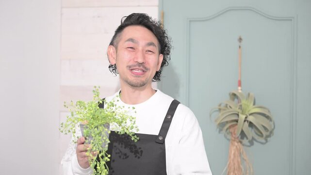 観葉植物を持つエプロン姿の男性　花屋や趣味の園芸イメージ　いらっしゃいませ～の動画