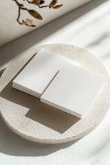 Two blank square cards on a round beige stone coaster, sunlit.