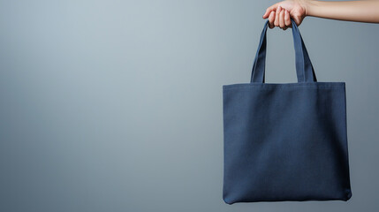 Hand holding up a blank blue tote bag on a solid light blue background for mockup purposes