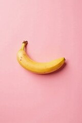 A single ripe yellow banana rests on a soft pink background, a vibrant and minimalist composition.