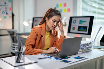 A woman in an orange jacket is working on a laptop computer