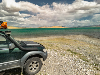 An off-road car with a solar panel stands against the background of dunes and a lake, overlooking the blue sky. Electric touring car with a view of Lake Barkhany and the sky. Off-road tires.
