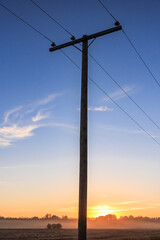 A tall wooden pole with power lines on it stands in a field