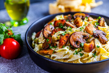 A delicious serving of creamy tagliatelle pasta topped with golden chicken and sautéed mushrooms, garnished with fresh parsley. Presented in a black bowl on a rustic background.