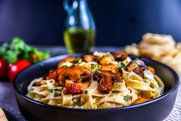 A delicious serving of creamy tagliatelle pasta topped with golden chicken and sautéed mushrooms, garnished with fresh parsley. Presented in a black bowl on a rustic background.
