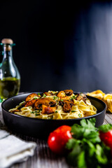 A delicious serving of creamy tagliatelle pasta topped with golden chicken and sautéed mushrooms, garnished with fresh parsley. Presented in a black bowl on a rustic background.