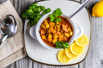 A hearty and flavorful stew featuring tender chickpeas, smoked sausage, and aromatic spices, garnished with fresh cilantro and served with lemon slices for a zesty finish.