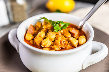 A hearty and flavorful stew featuring tender chickpeas, smoked sausage, and aromatic spices, garnished with fresh cilantro and served with lemon slices for a zesty finish.