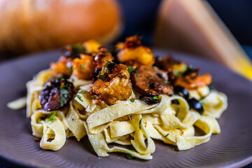 Creamy tagliatelle pasta topped with sautéed shrimp, mushrooms, and black olives, garnished with fresh herbs and Parmesan cheese.