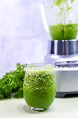 A refreshing glass of green juice prepared in a blender, featuring vibrant green parsley in the background. Perfect for a healthy lifestyle, this natural juice is packed with vitamins and flavor.

