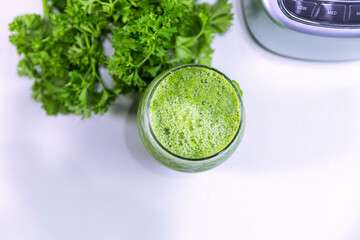 A refreshing glass of green juice prepared in a blender, featuring vibrant green parsley in the background. Perfect for a healthy lifestyle, this natural juice is packed with vitamins and flavor.

