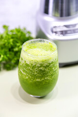 A refreshing glass of green juice prepared in a blender, featuring vibrant green parsley in the background. Perfect for a healthy lifestyle, this natural juice is packed with vitamins and flavor.

