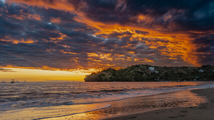 Fantastic flaming tropical sunset. Purple clouds are highlighted in scarlet and gold. The sky is orange on the horizon. Silhouettes of boats in the ocean. Foam waves on a sandy beach. Madagascar. 