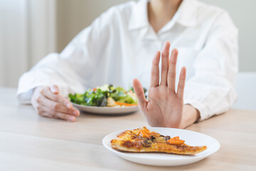 Diet concept, asian young woman close up hand push out away Pizza, refuse junk process, carb food on plate, choose green vegetable salad, eat low fat for good health. Female people getting weight loss