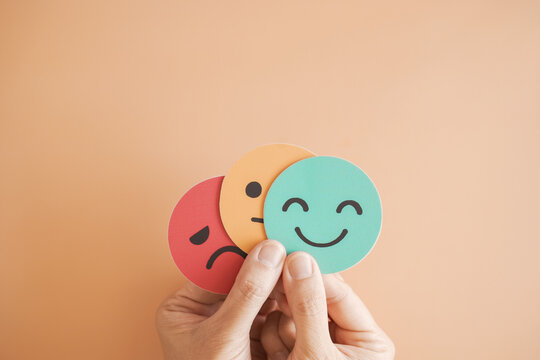 Hands holding sad face hiding behind happy face, bipolar and depression, mental health, split personality, mood change concept