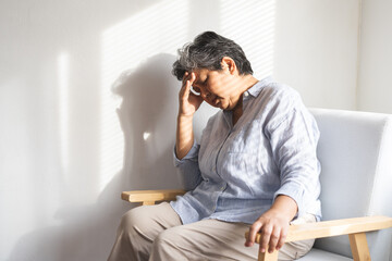 Unhappy asian elderly woman sitting on sofa at home, sick and stress headache feeling depressed...