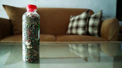 A clear plastic bottle with a red cap filled with colorful hamster food,  seeds, pellets, and dried...