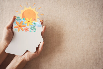 Hands holding paper brain with flowers and sunshine, positive mental health, mindfulness, wellness,...