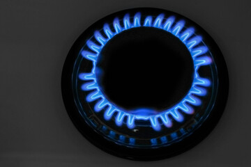 Gas burner of modern stove with burning blue flame at night, closeup