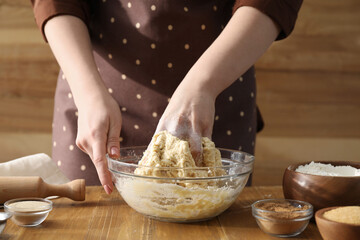 Woman kneading dough for cinnamon rolls at wooden table, closeup