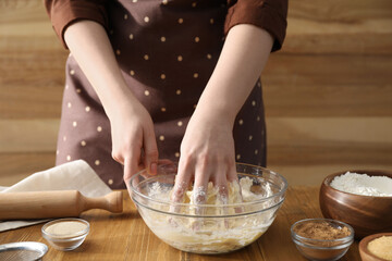 Woman kneading dough for cinnamon rolls at wooden table, closeup