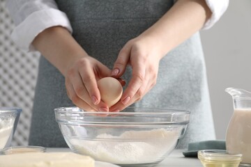Making cinnamon rolls. Woman adding egg into bowl at table, closeup