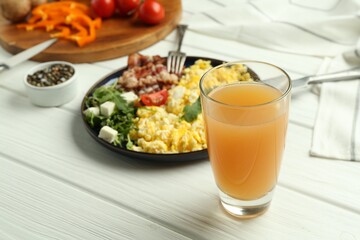 Tasty brunch. Glass of apple juice and scrambled eggs with bacon served on white wooden table, closeup