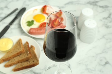 Tasty brunch. Glass of red wine, fried egg, sausage, bread and sauce on white marble table, closeup