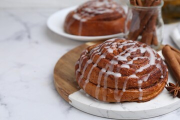 Tasty cinnamon roll with cream and spices on white marble table, closeup
