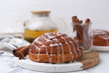 Tasty cinnamon roll with cream and spices on white marble table, closeup