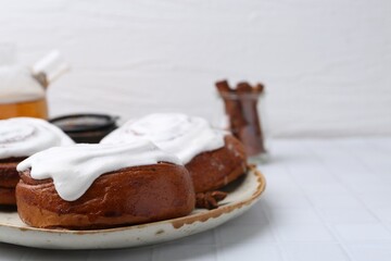 Tasty cinnamon rolls with cream and spices on white tiled table, closeup. Space for text
