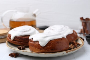 Tasty cinnamon rolls with cream and spices on white tiled table, closeup. Space for text