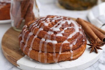 Tasty cinnamon roll with cream and spices on white marble table, closeup