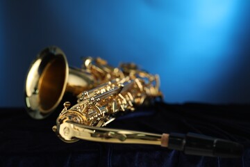 Jazz. One beautiful saxophone on dark fabric against light blue background, closeup. Space for text