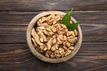 Peeled walnuts and green leaves in bowl on wooden table, top view