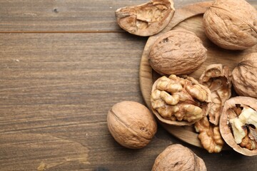 Fresh walnuts with shells on wooden table, flat lay. Space for text