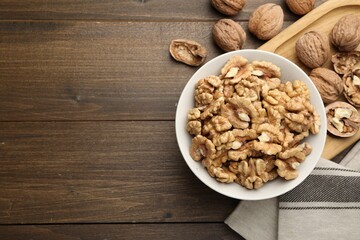 Peeled walnuts in bowl on wooden table, flat lay. Space for text