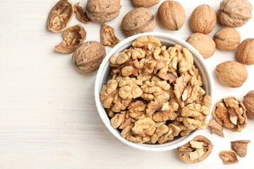 Peeled walnuts in bowl and whole ones on light wooden table, flat lay. Space for text