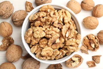 Peeled walnuts in bowl and whole ones on light table, flat lay