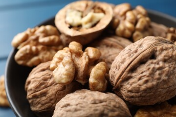 Fresh walnuts in bowl on blue table, closeup